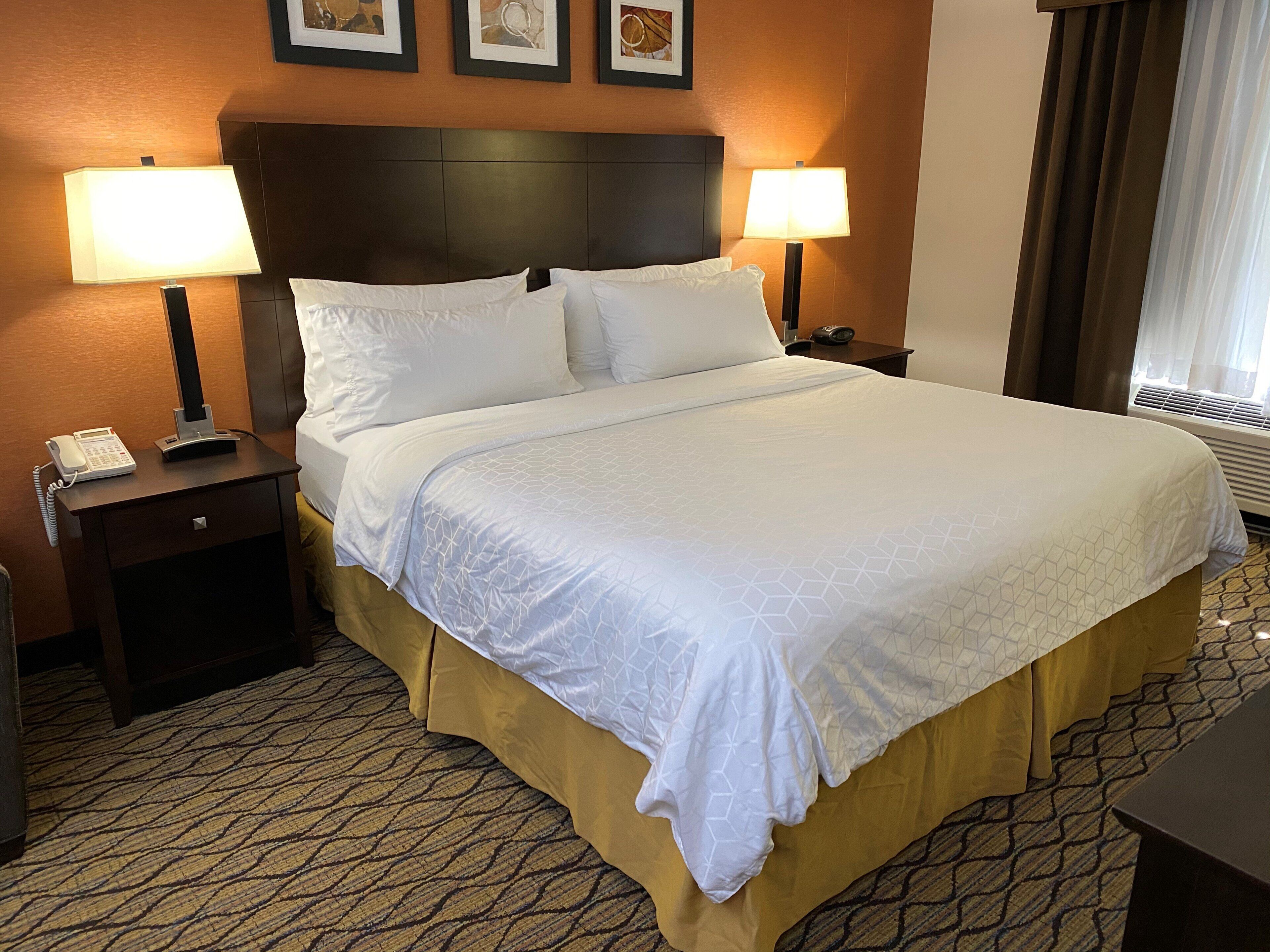 A hotel room with a large bed, two bedside lamps, a telephone on the nightstand, and a framed picture on the wall.