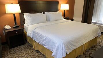 A hotel room with a large bed, two bedside lamps, a telephone on the nightstand, and a framed picture on the wall.