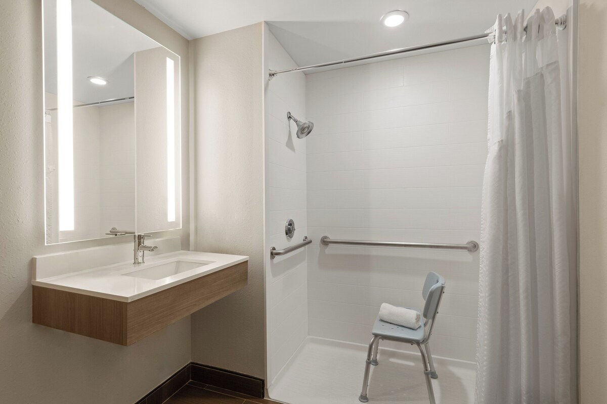 A bathroom with a shower, a sink, and a chair.