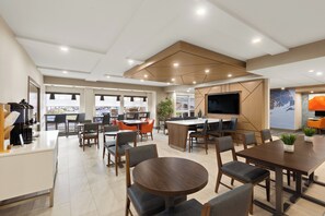 A modern dining area with round tables and chairs, a large TV, and a view of the city through large windows. - Holiday Inn Express Hotel & Suites Danbury - I-84 by IHG (Danbury)