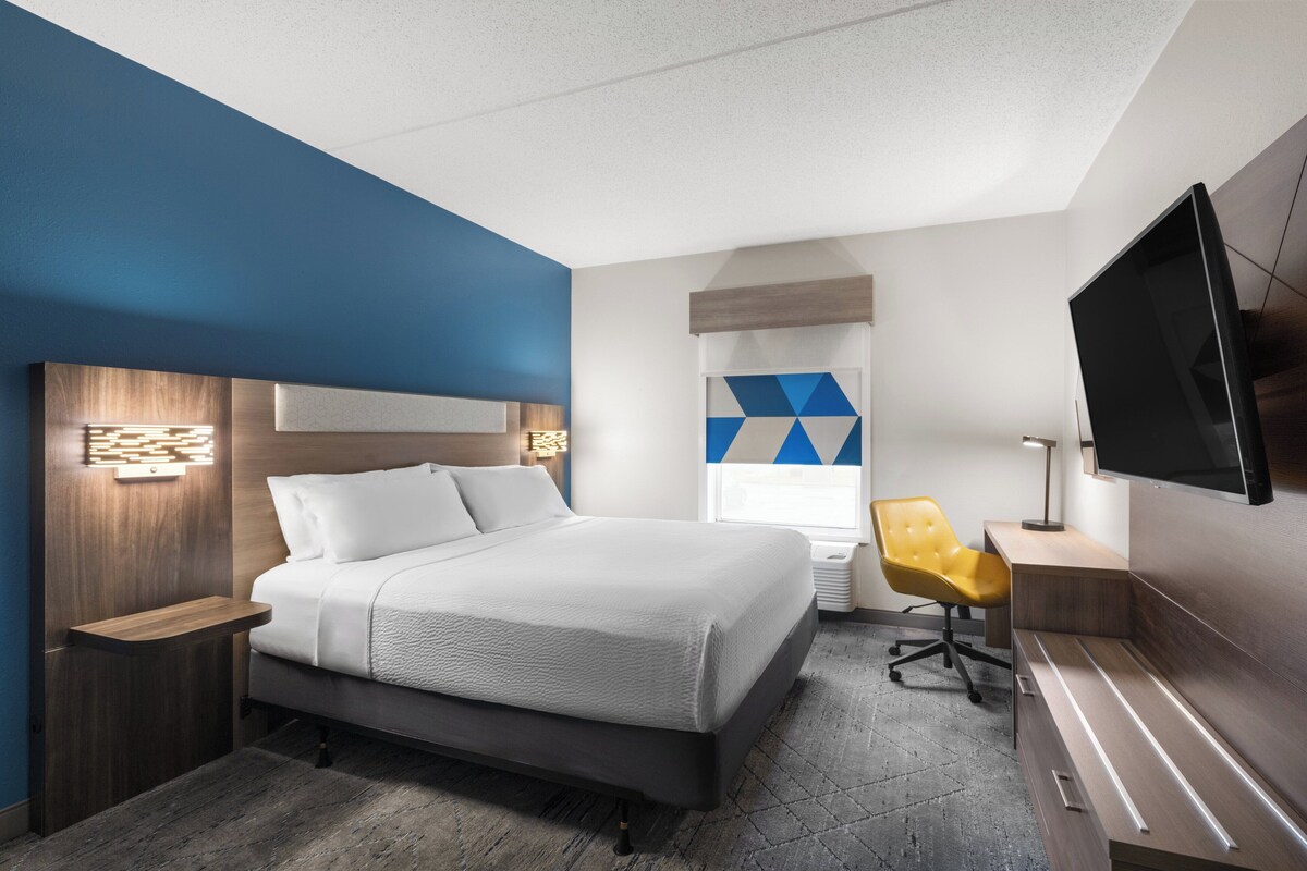 A modern hotel room with a large bed, a desk, a chair, and a flat-screen TV.