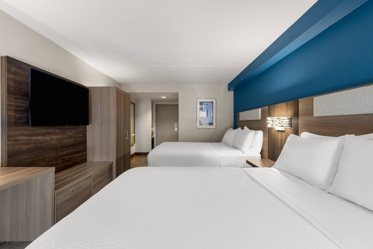 Ein Hotelzimmer mit zwei Betten, einem Flachbildfernseher, Holzmöbeln und einer blauen Wand.