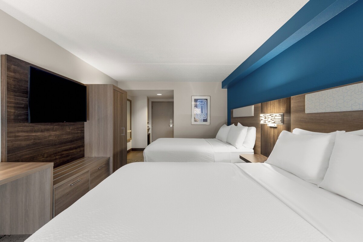 A hotel room with two beds, a flat-screen TV, wooden furniture, and a blue accent wall.