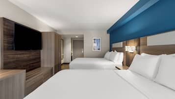Habitación de hotel con dos camas, televisión de pantalla plana, muebles de madera y una pared decorada en tono azul.