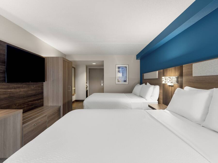 Habitación de hotel con dos camas, televisión de pantalla plana, muebles de madera y una pared decorada en tono azul.