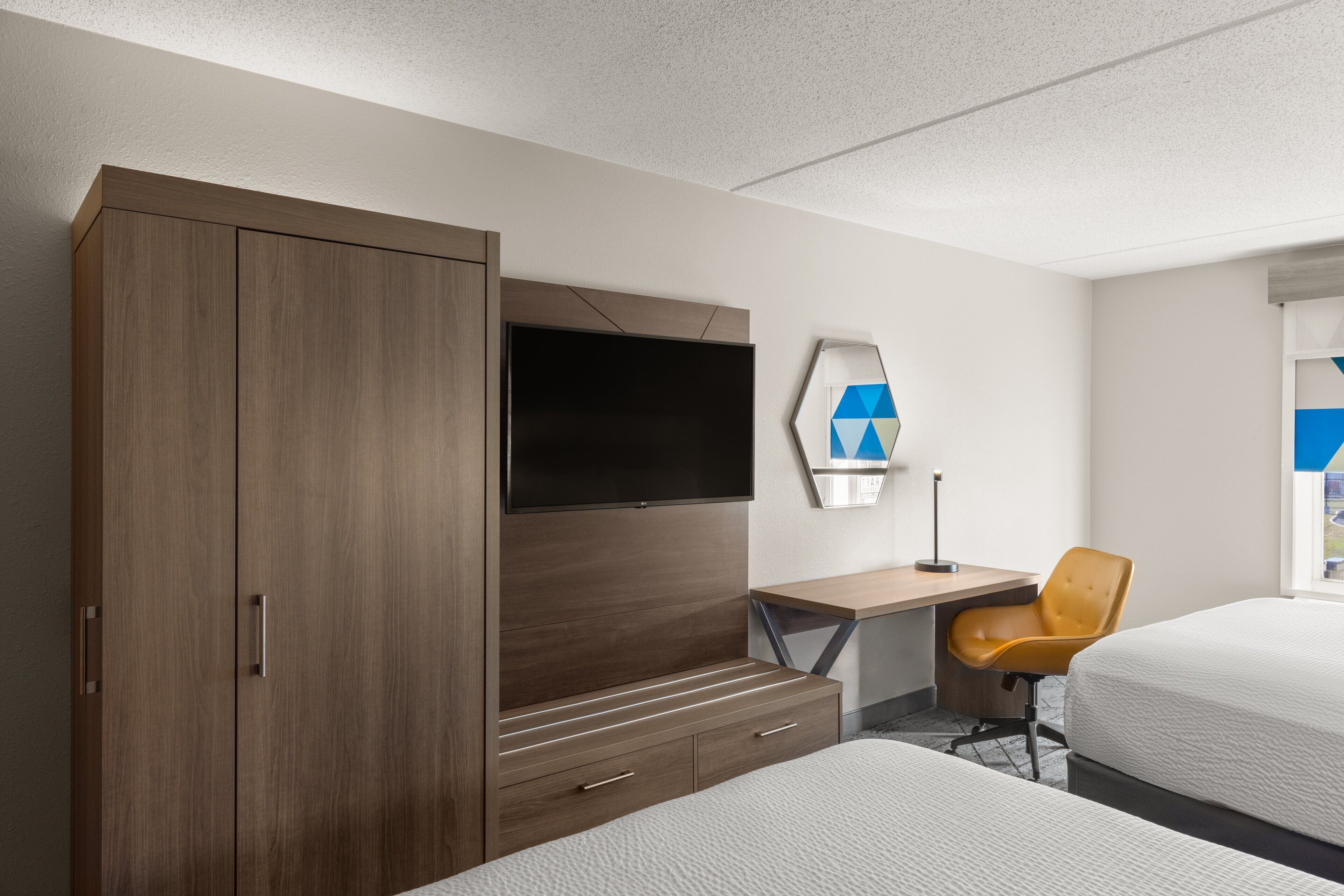 Habitación de hotel con un armario grande, un televisor de pantalla plana, un escritorio con silla y dos camas.