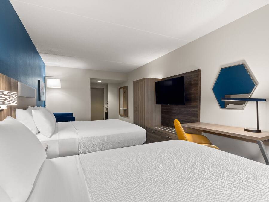 Habitación de hotel con dos camas, un escritorio, una silla, un televisor y una lámpara fijada a la pared.