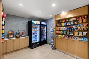 A self-service snack and beverage area with refrigerated drink dispensers and shelves stocked with various snacks and beverages. - Holiday Inn Express Hotel & Suites Danbury - I-84 by IHG (Danbury)