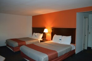 A hotel room with two beds, each with a wooden headboard, a nightstand with a lamp, and a door to the right.