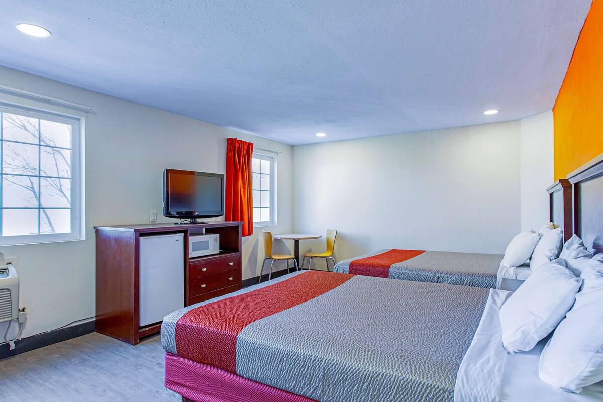 A hotel room with two beds, a desk, a television, and a window with curtains.
