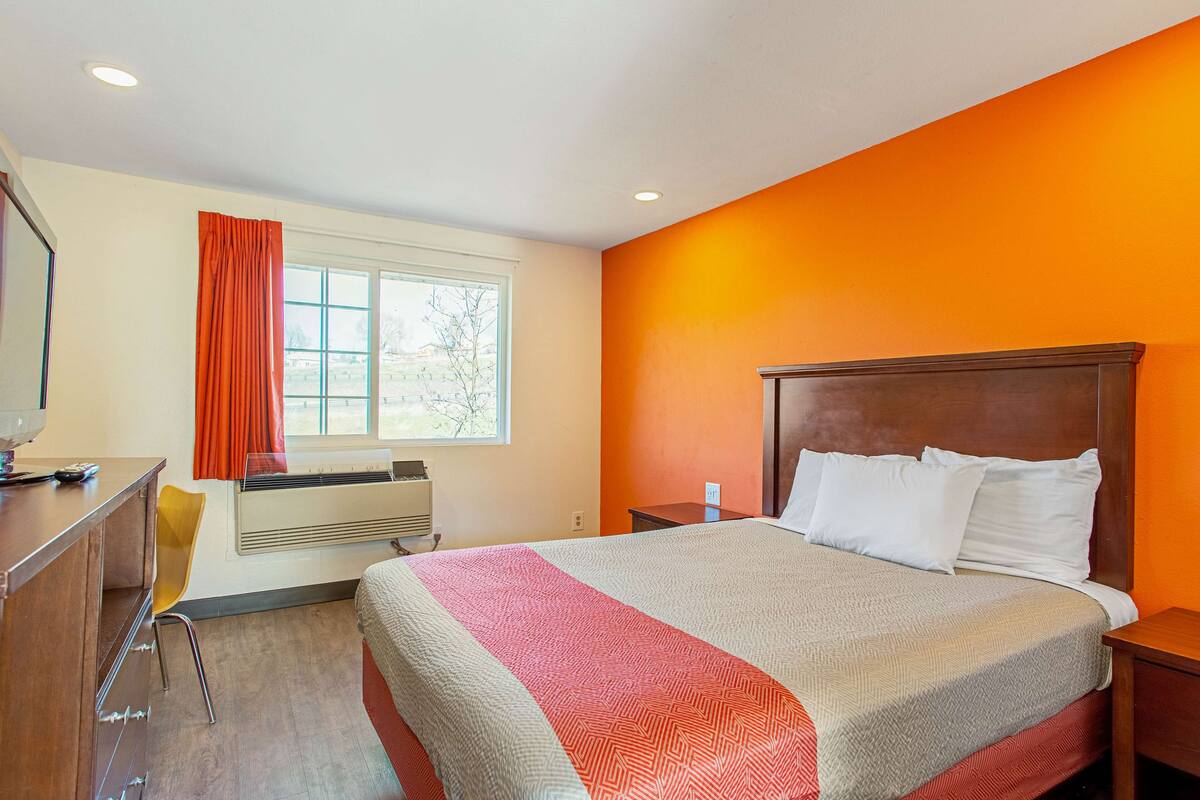 A hotel room with a bed, a desk, a chair, and a window with curtains.