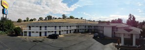A motel with a central parking area, a small building with a red roof, and a sign for 'Denny's' in the background.