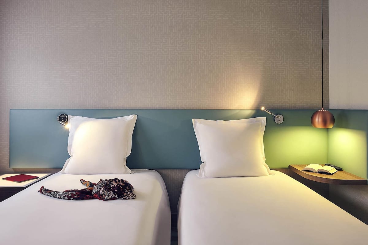 Une chambre d’hôtel avec deux lits, une table de chevet avec une lampe et une petite table avec un livre et une télécommande.