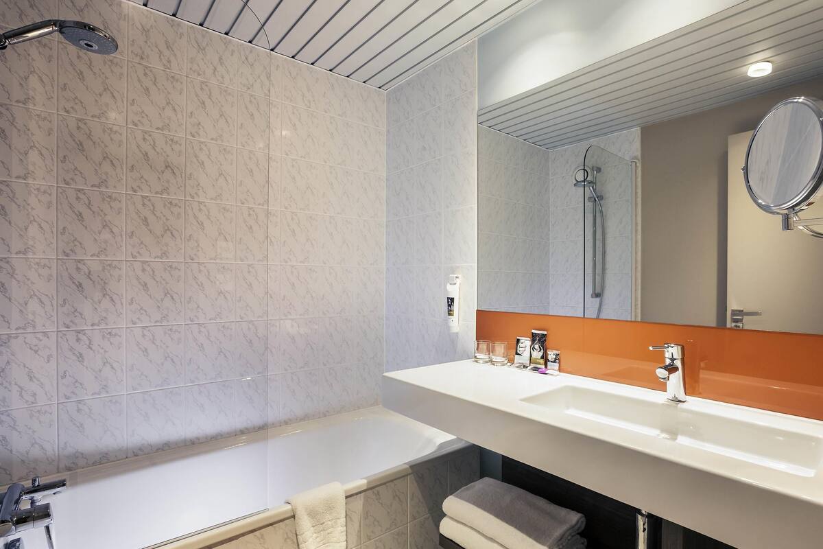 A modern bathroom with a bathtub, a large mirror, and a sink.