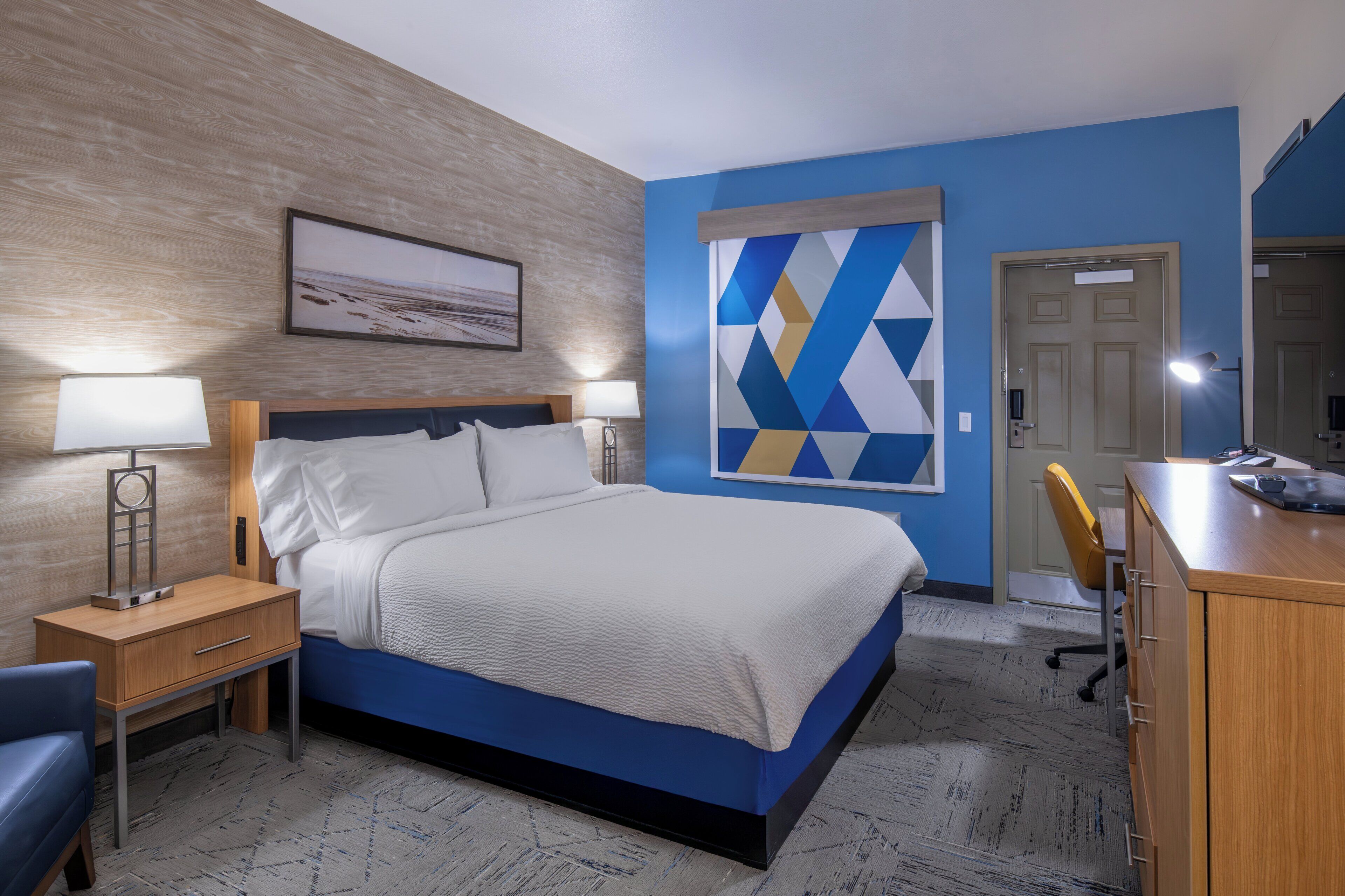 A hotel room with a bed, bedside tables, a desk, and a chair.