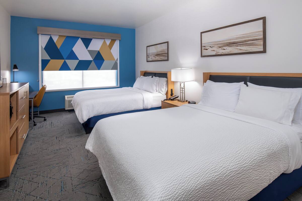 A hotel room with two beds, a desk, a chair, and a window with blinds.