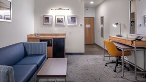 A hotel room with a sofa, a desk, a chair, a small table, a kitchenette, and a mirror. - Holiday Inn Express Hotel & Suites Henderson by IHG (Henderson)