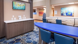 A hotel lobby with a reception desk, a blue conference table, and two blue chairs. - Holiday Inn Express Hotel & Suites Henderson by IHG (Henderson)