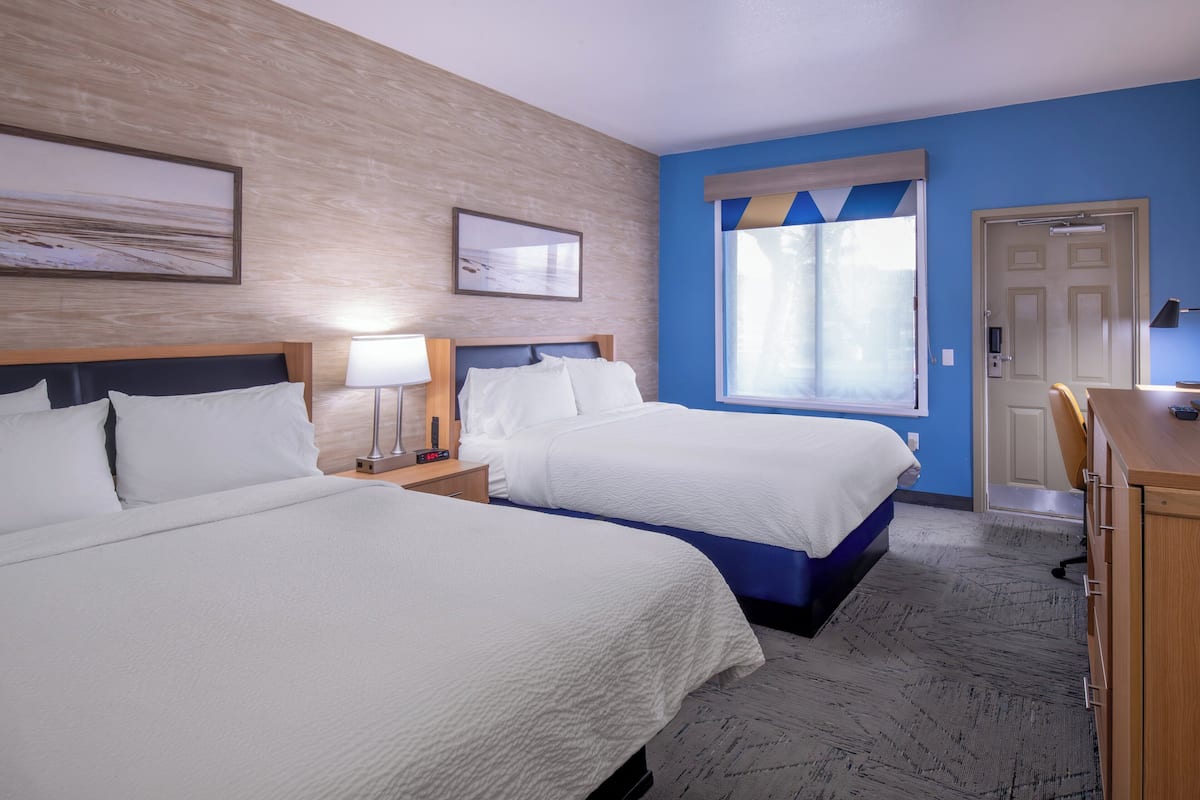 A hotel room with two beds, a desk, a chair, and a window with curtains.
