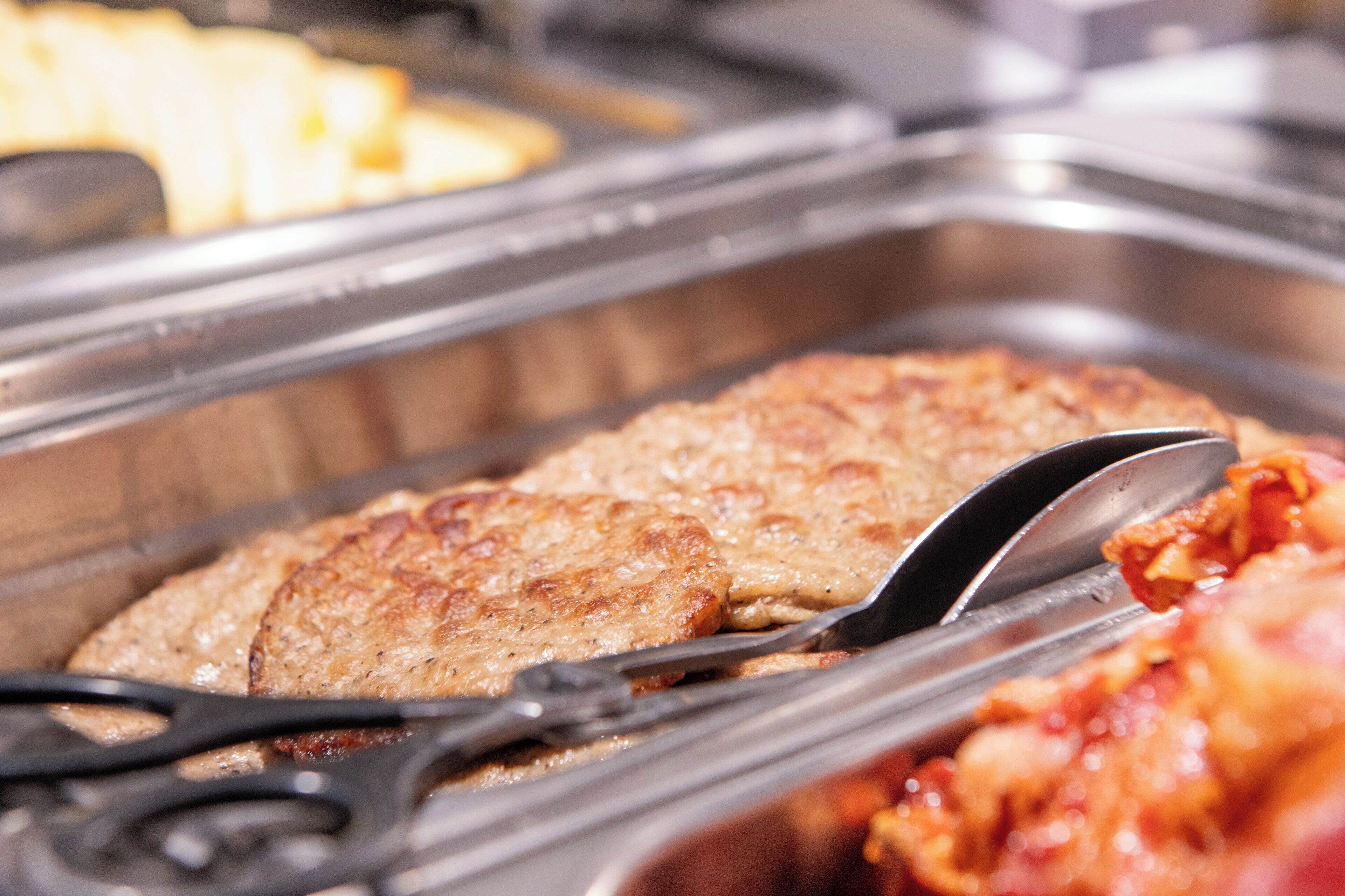 Buffet com diversos pratos, incluindo um pedaço de carne grelhada e um recipiente com molho.