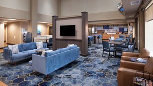 A hotel lobby with a blue sofa set, a flat-screen TV, and a dining area with tables and chairs. - Holiday Inn Express Hotel & Suites Henderson by IHG (Henderson)