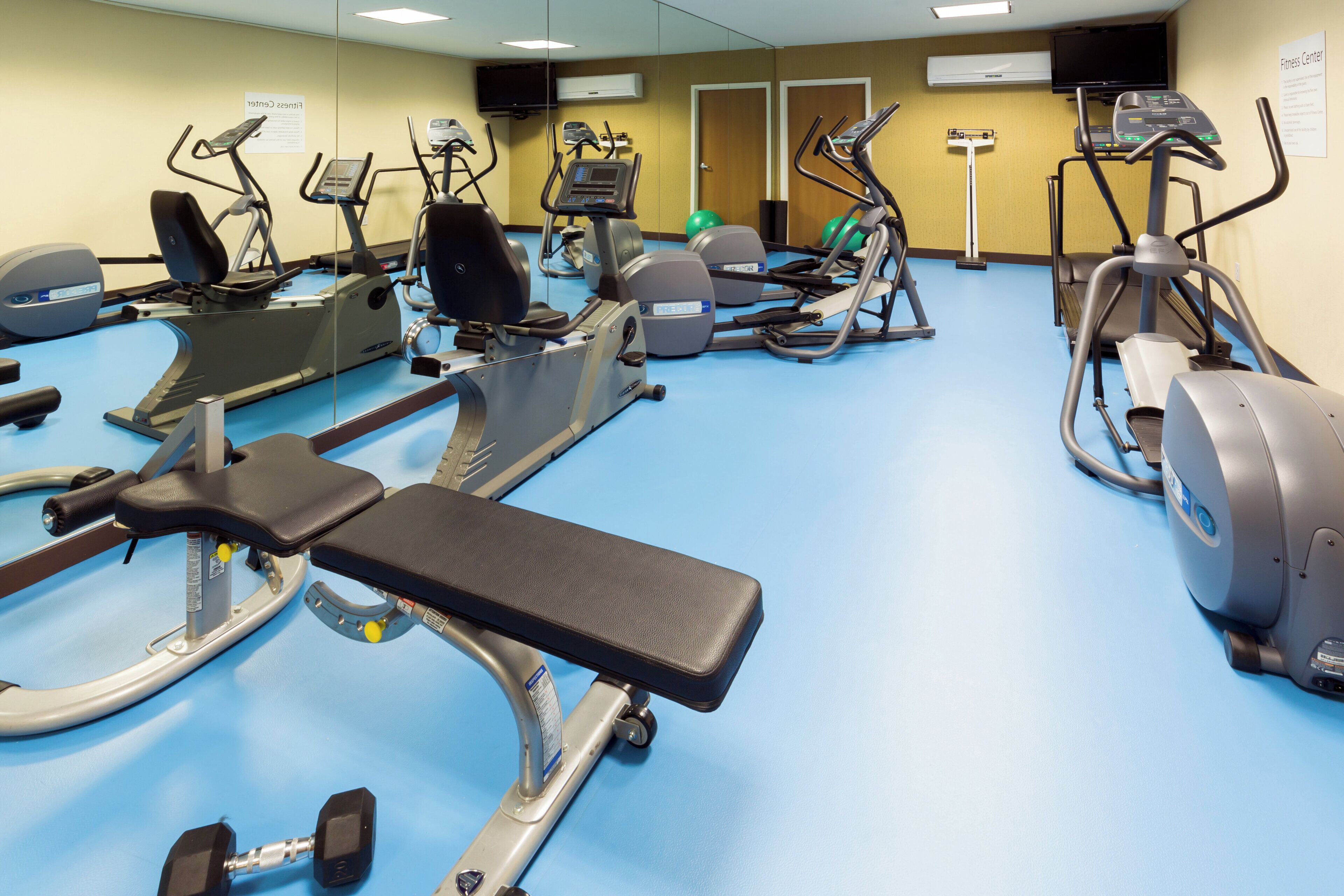 A fitness center with various exercise equipment including treadmills, elliptical machines, and a bench.