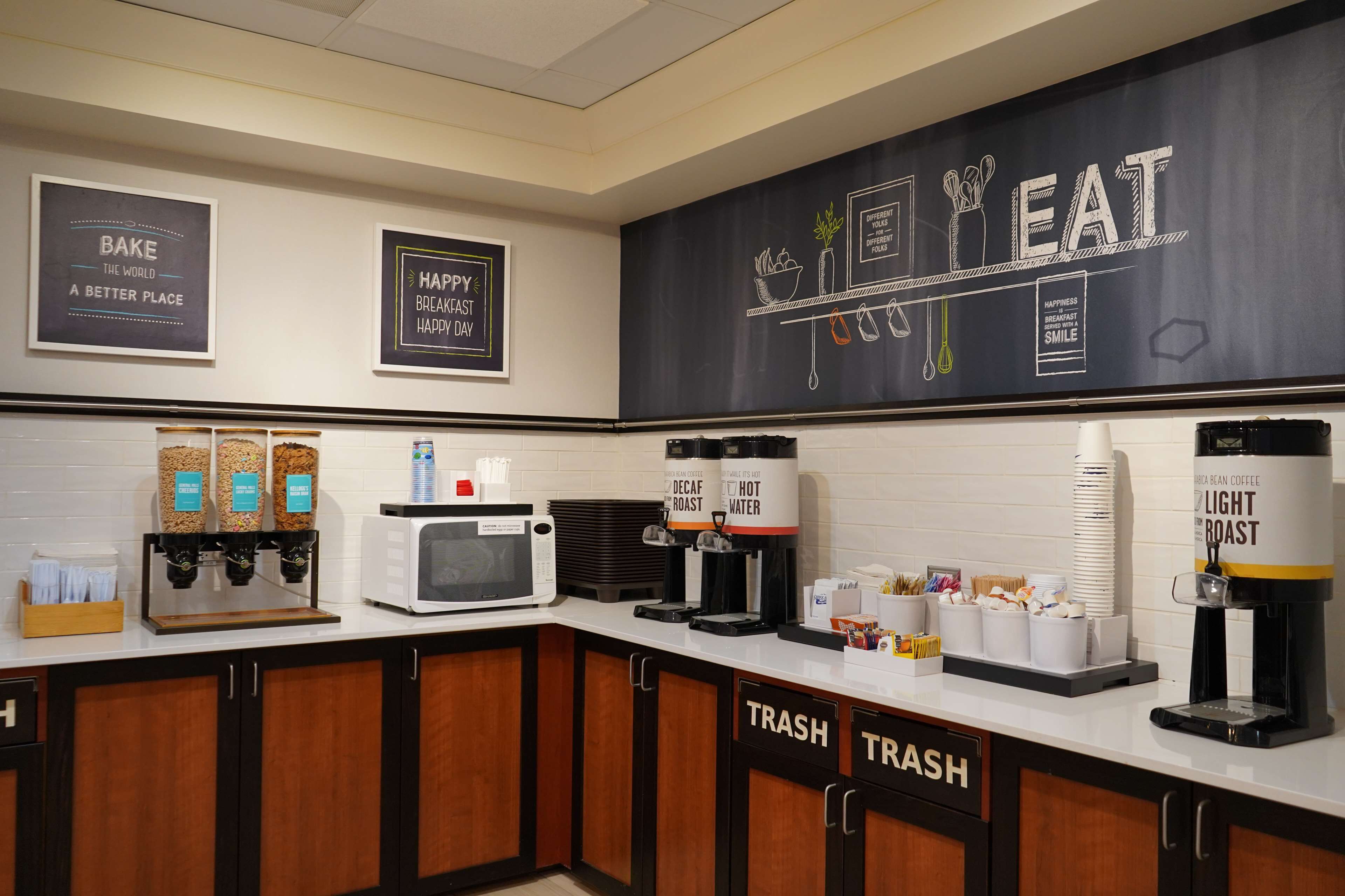 A kitchen area with coffee machines, a microwave, and labeled trash bins.