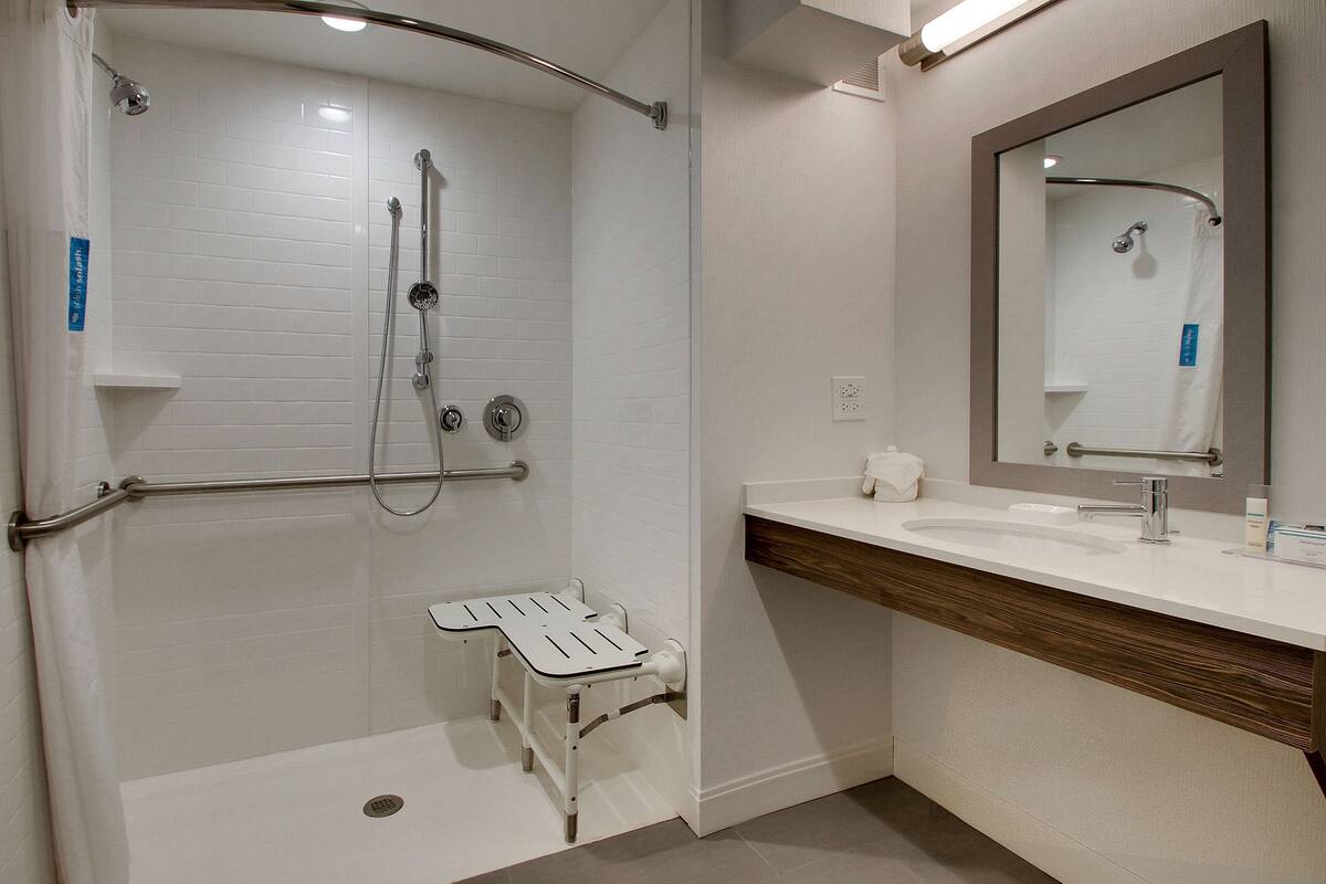 Un baño moderno con cabina de ducha, tocador con espejo y un pequeño taburete para facilitar el acceso.