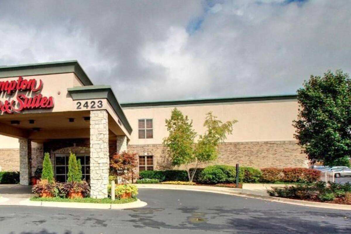 Un hotel Hampton Inn & Suites con fachada de piedra, un acceso cubierto y un estacionamiento.