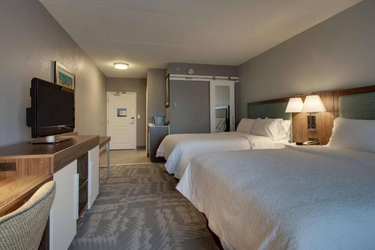 Habitación de hotel con cama, escritorio con televisor, mesita de noche con lámpara y puerta que da a un baño.