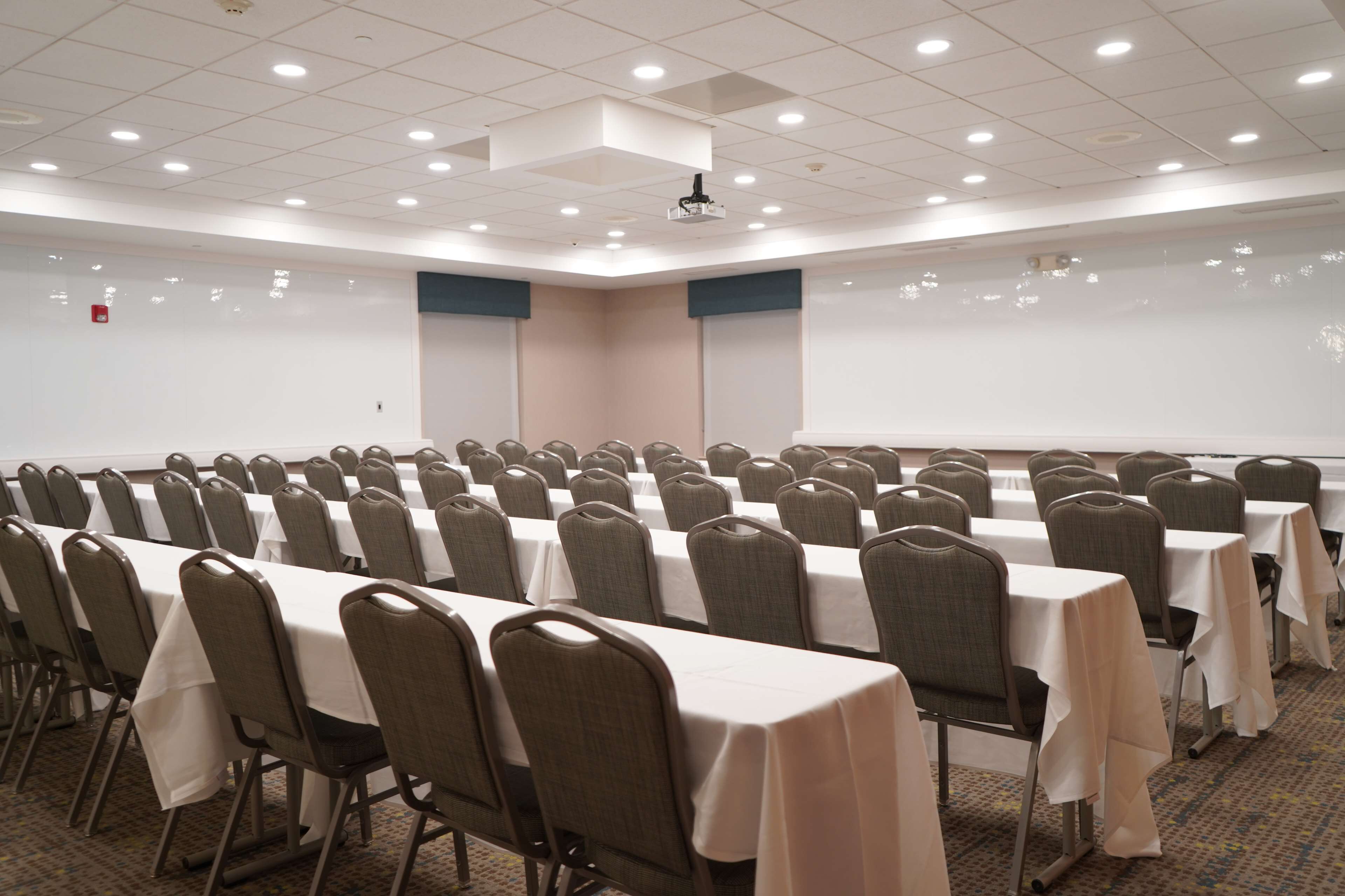 A conference room with rows of tables and chairs, a whiteboard, and a projector on the ceiling.