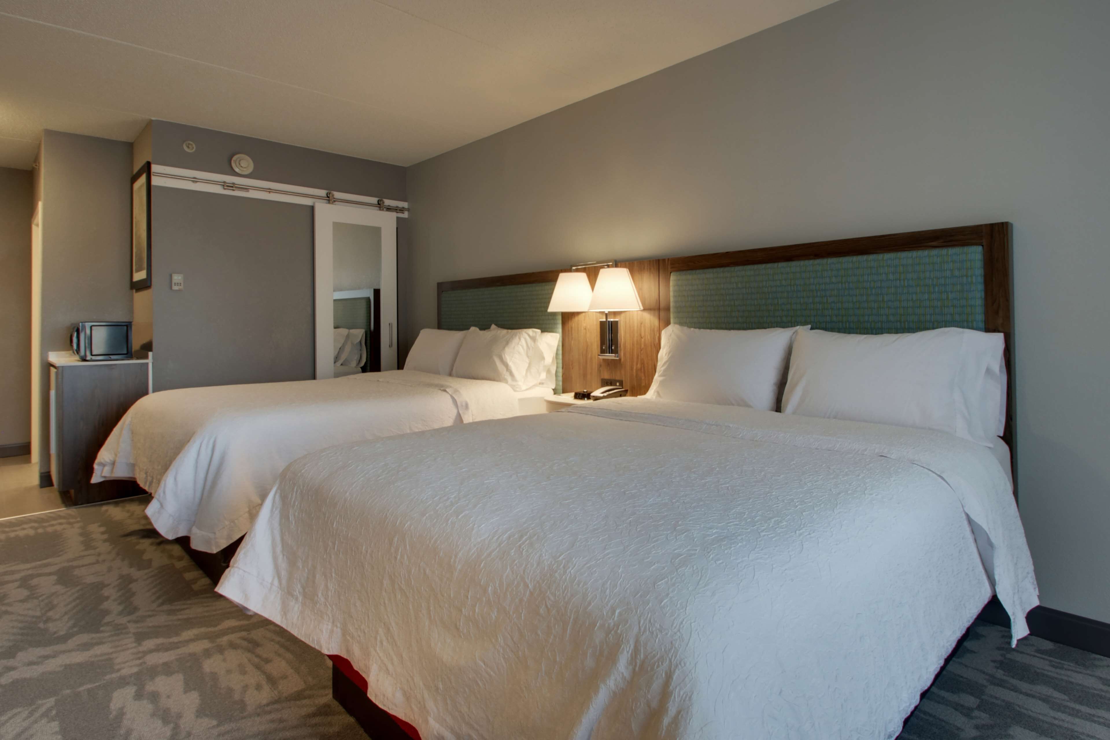 A hotel room with two beds, a bedside table with a lamp, a mirror, and a television.