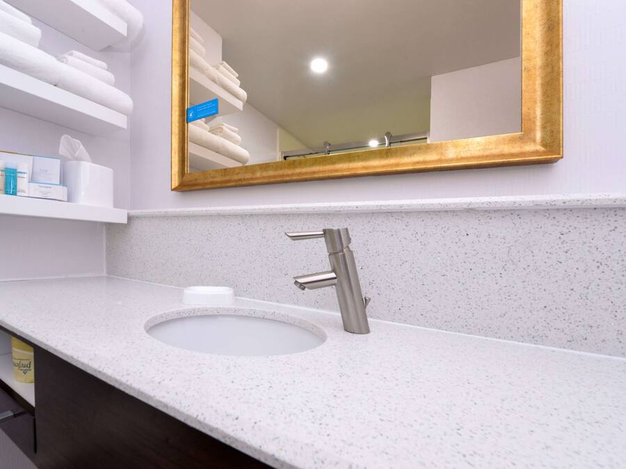 A bathroom with a white sink, a gold-framed mirror, and shelves with towels and toiletries.