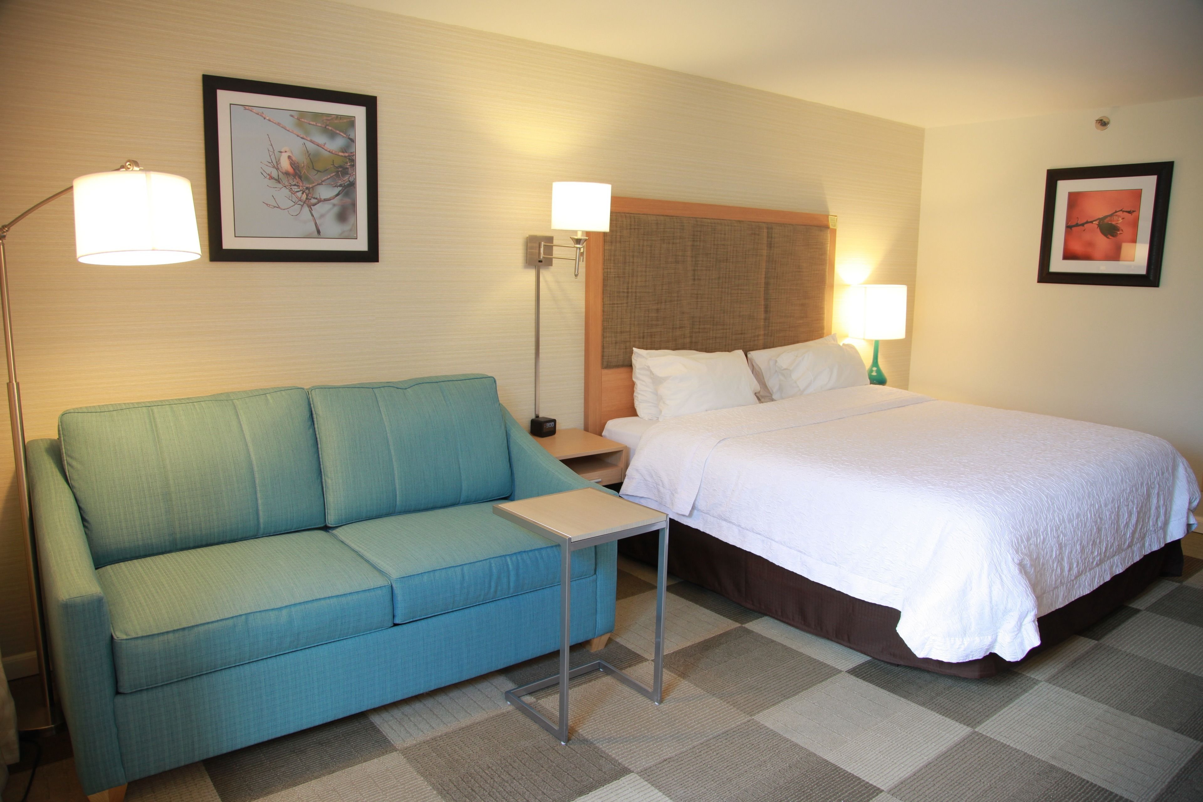 A hotel room with a bed, a sofa, a small table, and two wall-mounted lamps.