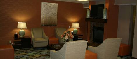 Una habitación de hotel con chimenea, dos sillones, un sofá y una alfombra estampada.