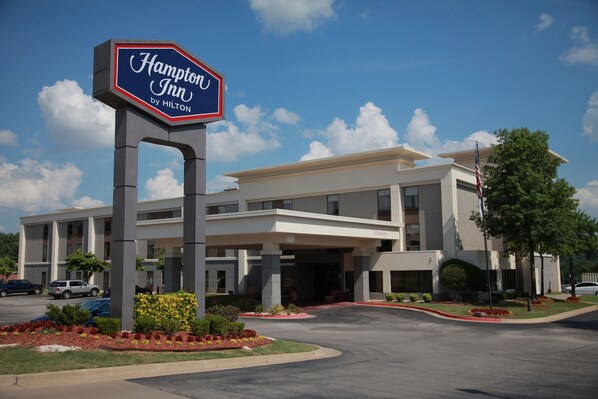 Ein Hampton Inn by Hilton Hotel mit modernem Design, einladendem Eingangsbereich und einem begrünten Zufahrtsweg.