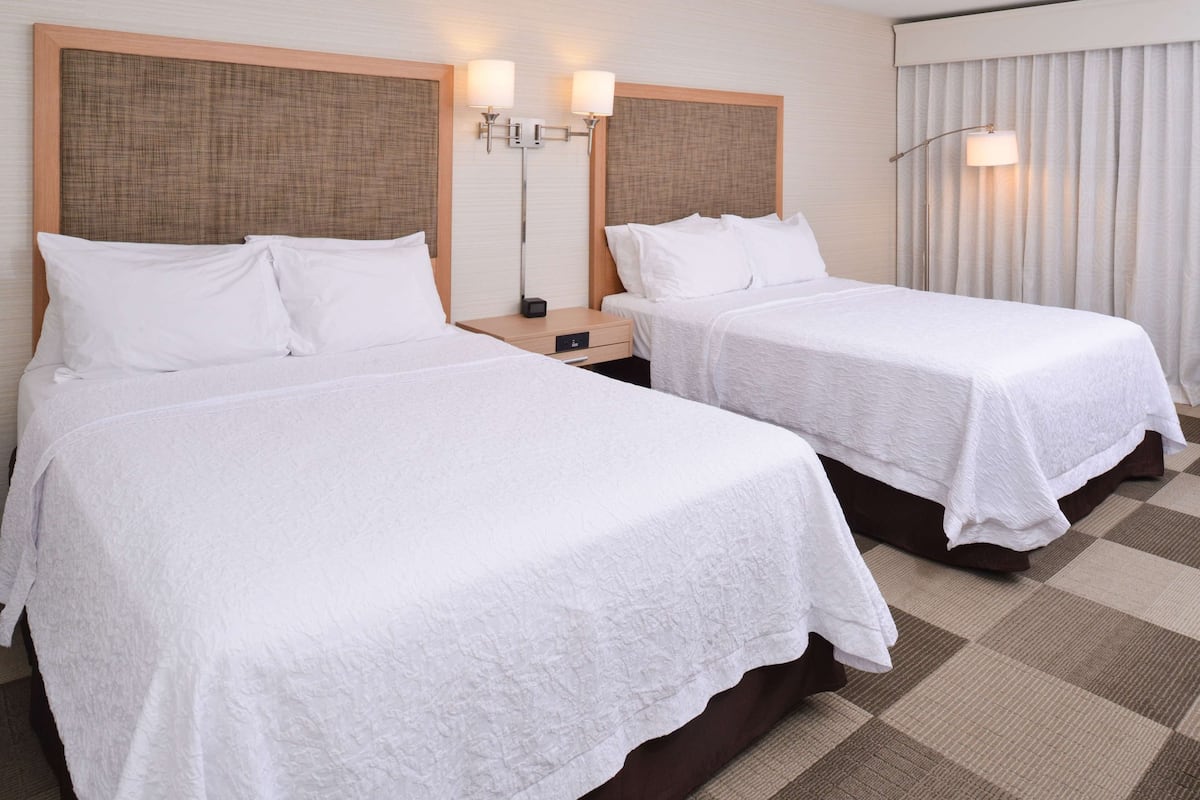 A hotel room with two single beds, a nightstand, a lamp, and a window with curtains.