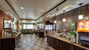 A hotel lobby with a checkered floor, a buffet area with various food items, and a juice bar. - Hampton Inn Tulsa-Sand Springs (Tulsa)