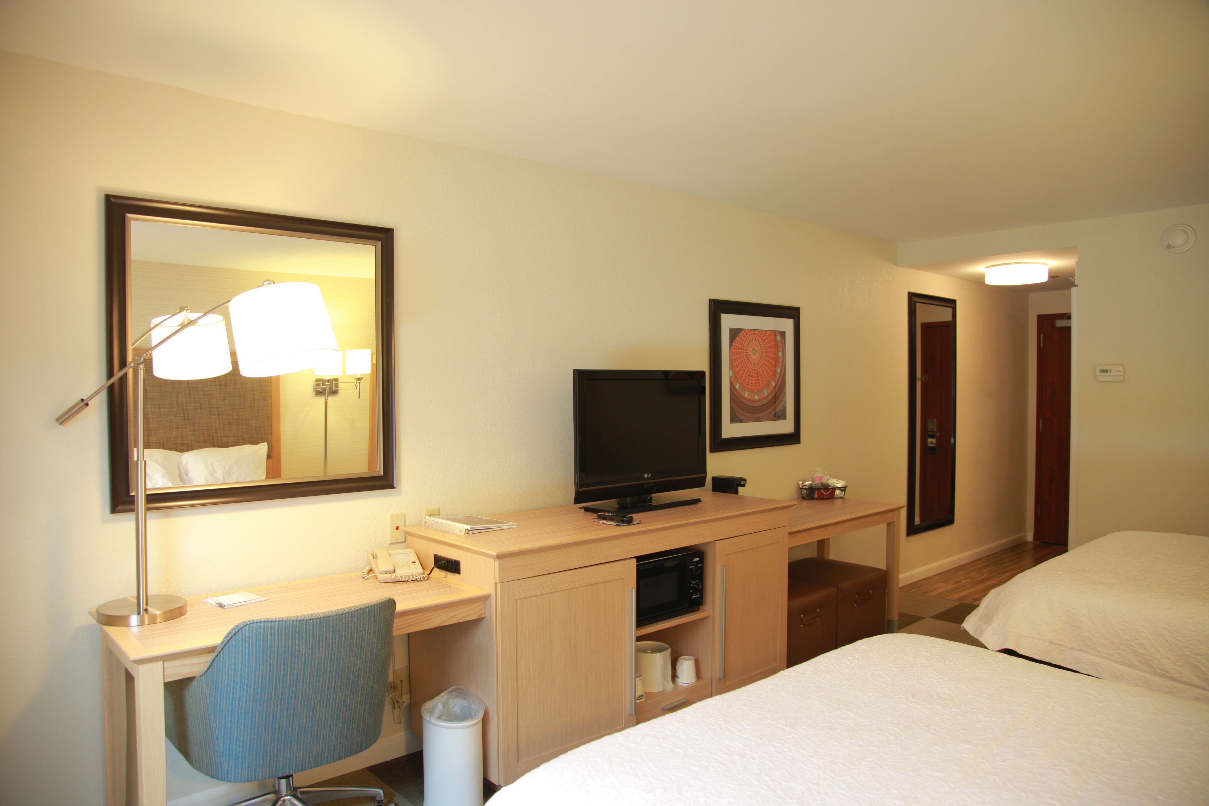 Une chambre d’hôtel équipée d’un lit, d’un bureau avec un ordinateur, d’une chaise, d’une télévision et d’un miroir.