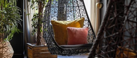 Una habitación con una silla colgante, una planta en maceta y un contenedor de madera.