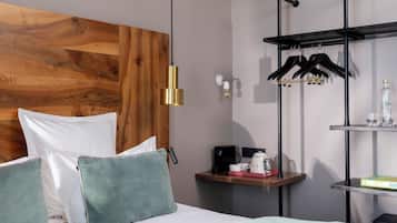 A modern bedroom with a wooden headboard, a bed with green and white bedding, a nightstand with a coffee maker, and a black hanger rack.