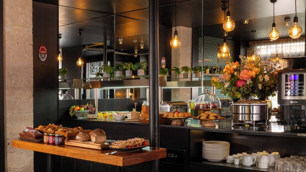 A buffet area with various food items, a coffee station, and a decorative flower arrangement.