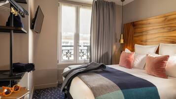 Habitación de hotel con cama, ventana con cortinas, perchero y vista a edificios.