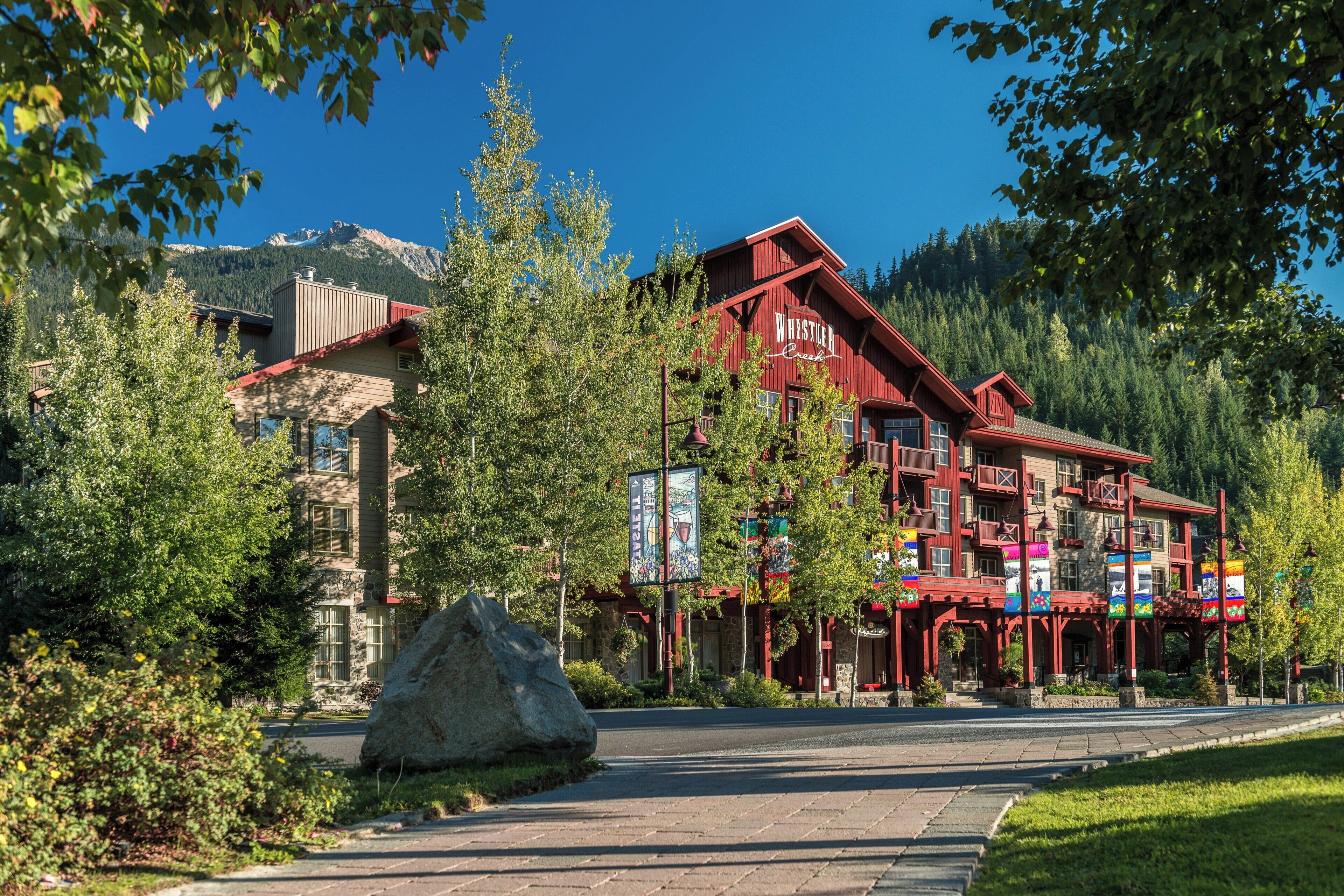 A red building with 'Whistler Creek' signage, surrounded by trees and a mountain backdrop.