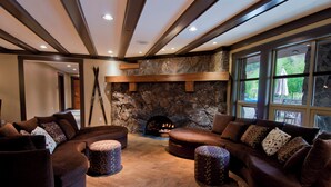 A modern living room with a stone fireplace, leather sofas, and a large window. - Legends Whistler, by Lodging Ovations (Whistler)