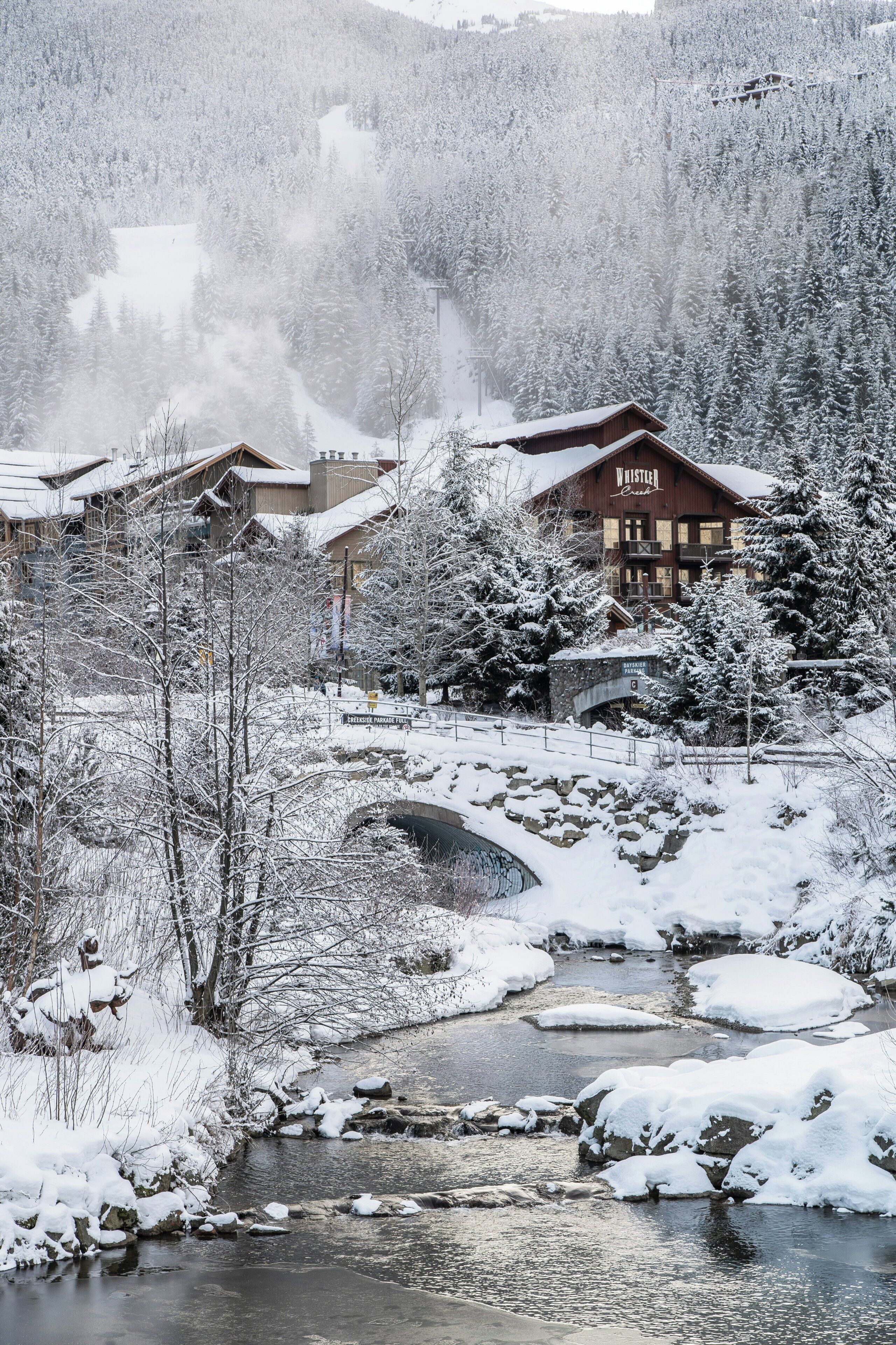 Una cabaña con fachada de madera, un puente de piedra y un paisaje cubierto de nieve.