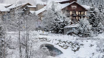 Una cabaña con fachada de madera, un puente de piedra y un paisaje cubierto de nieve.
