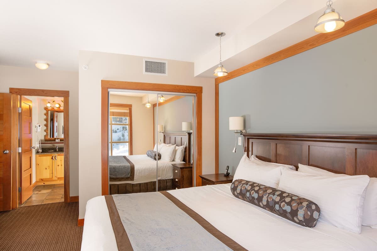 A hotel room with a large bed, a wooden headboard, a bedside table, and a mirror.