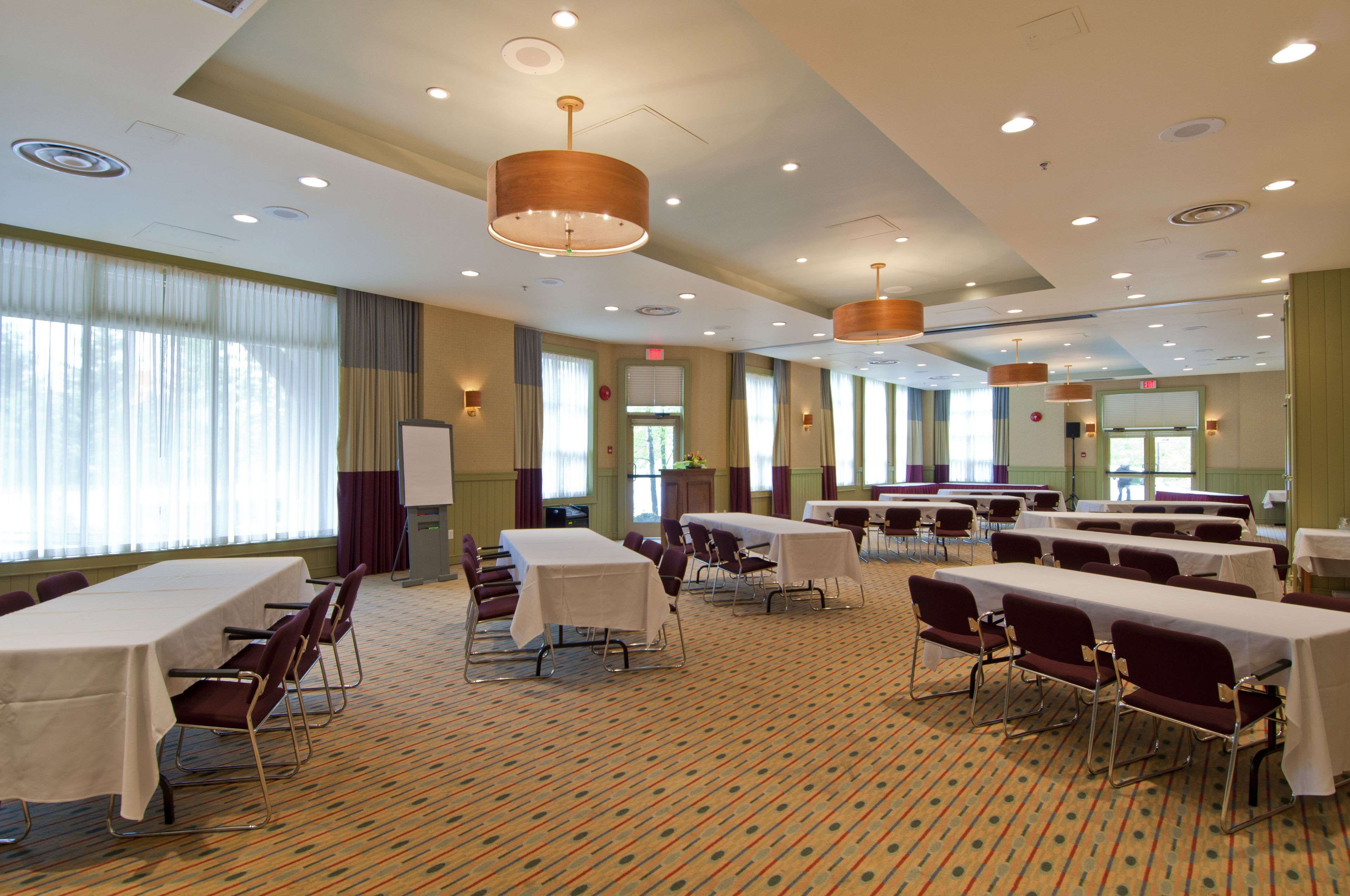 A conference room with multiple tables and chairs, large windows with curtains, and ceiling lights.