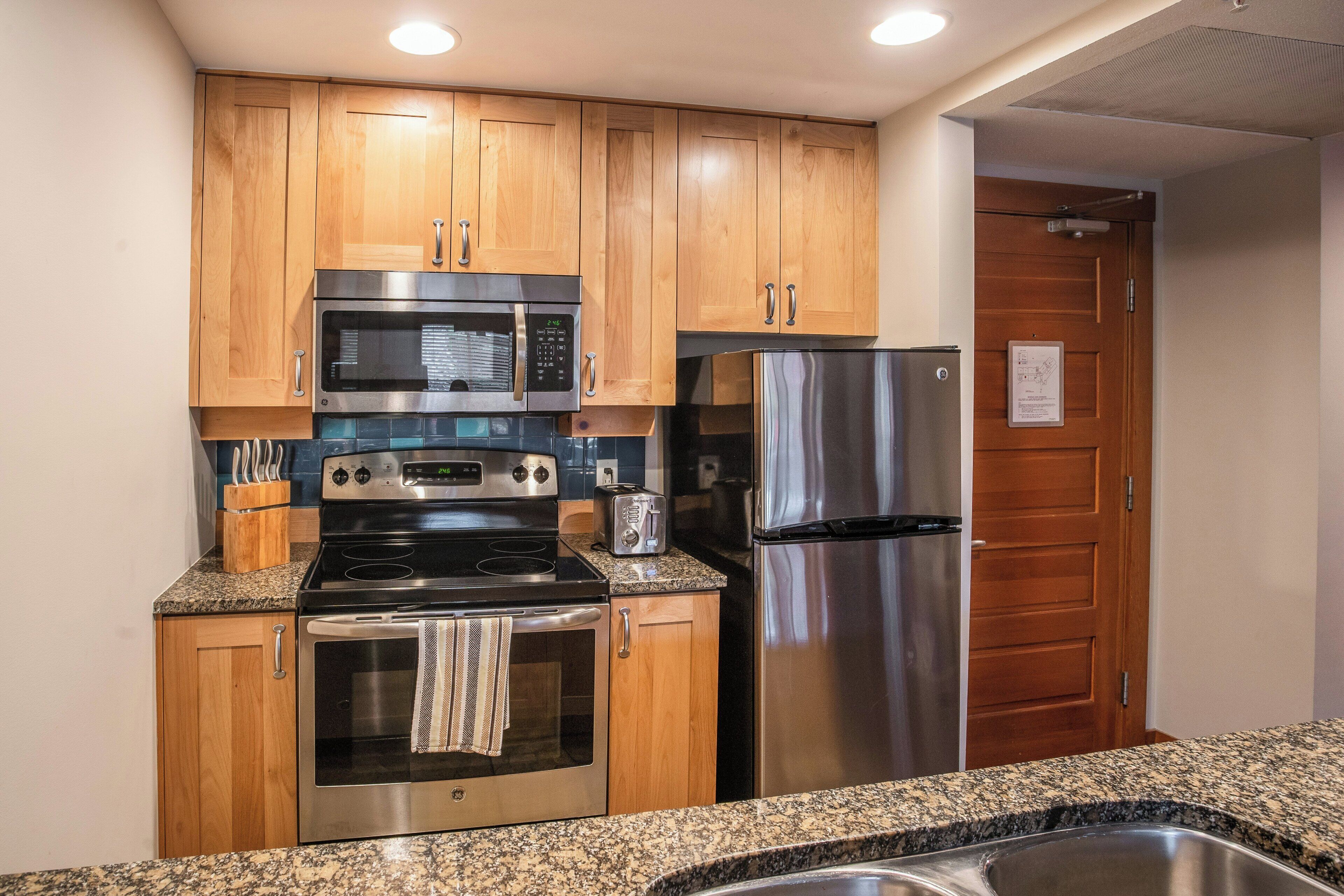 A kitchen with wooden cabinets, stainless steel appliances, granite countertops, and a stainless steel sink.
